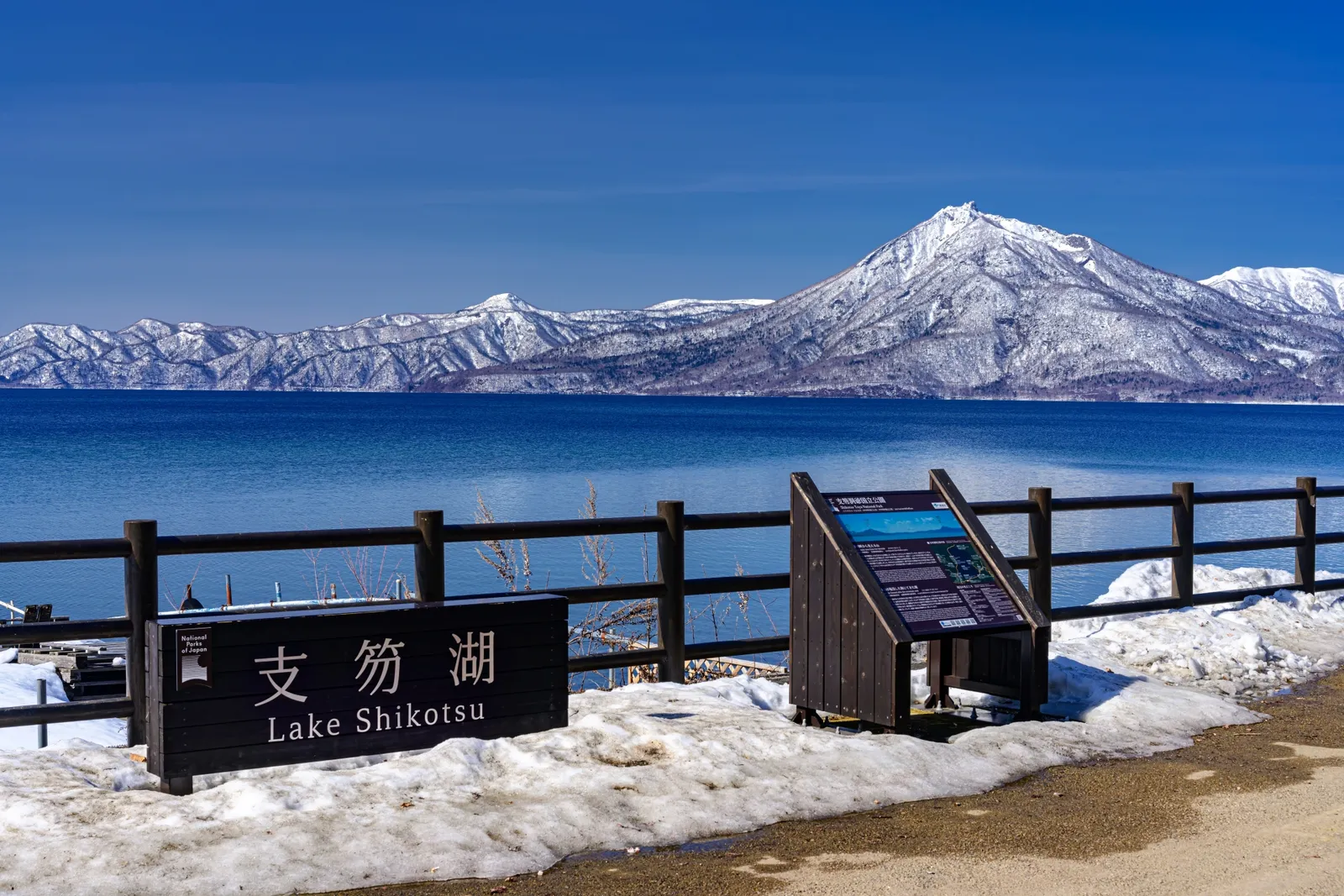 雪の残る支笏湖の湖畔から眺める青い湖面と雪山
