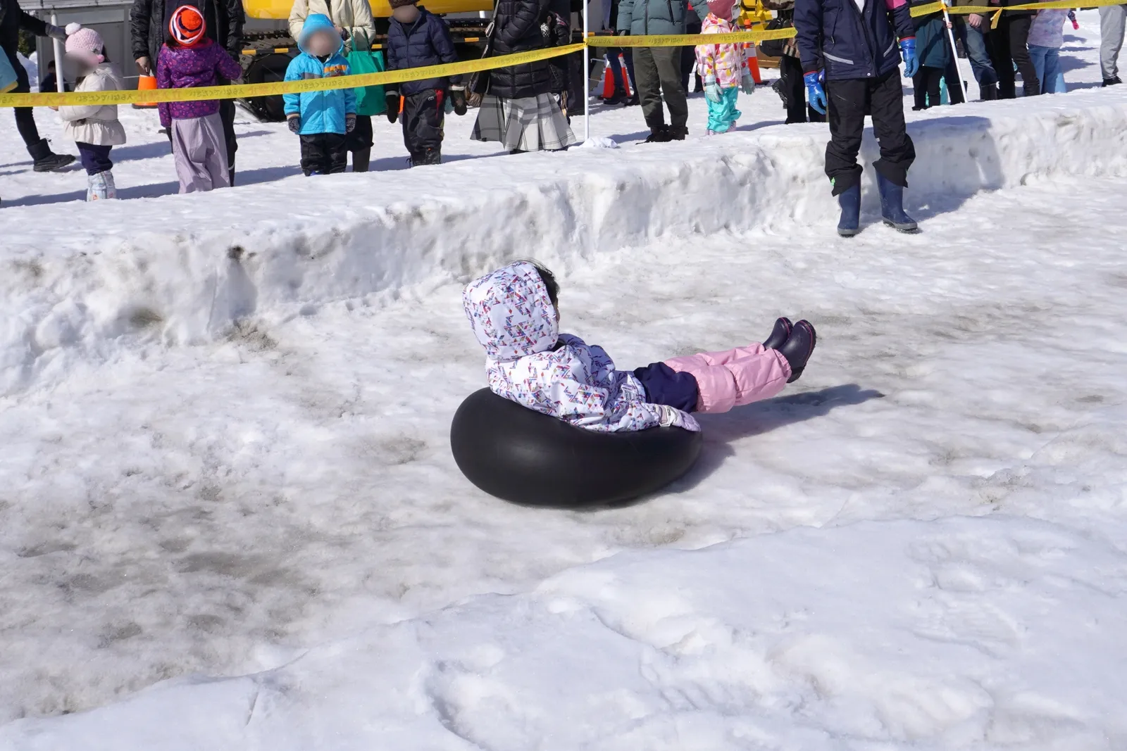 雪の斜面をスノーチューブで滑る子ども