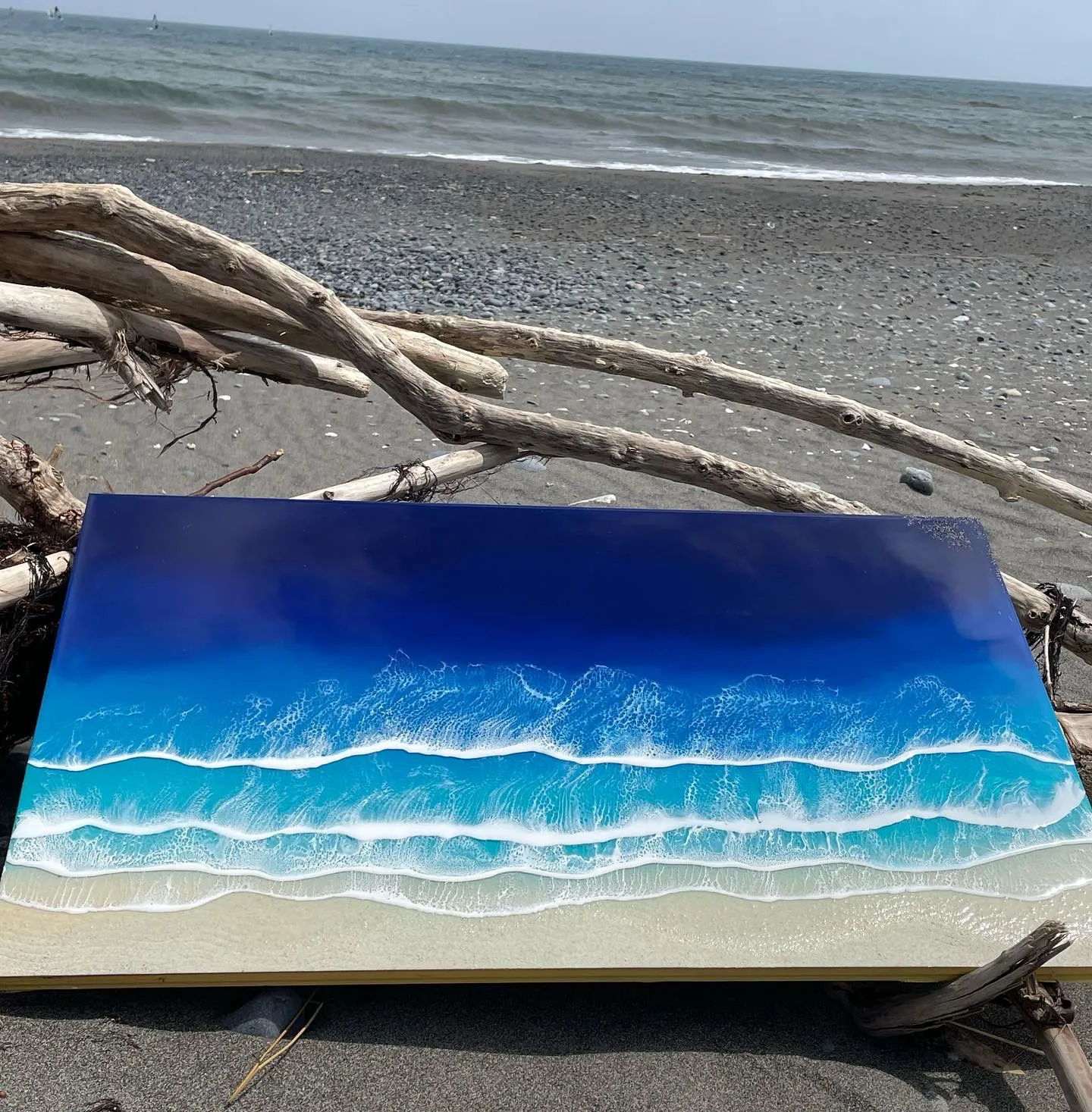 流木のそばに置かれた、青い海と幾重もの白い波を表現した横長のレジンアート