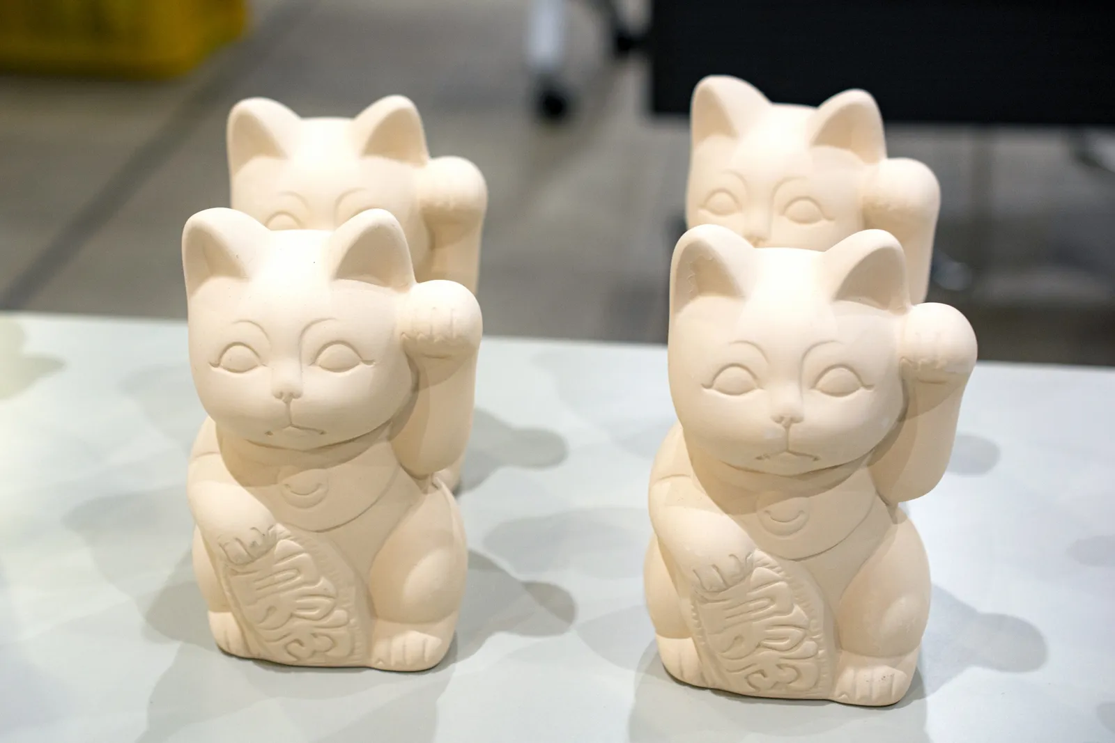 Unpainted maneki-neko, each holding a koban coin and raising one paw