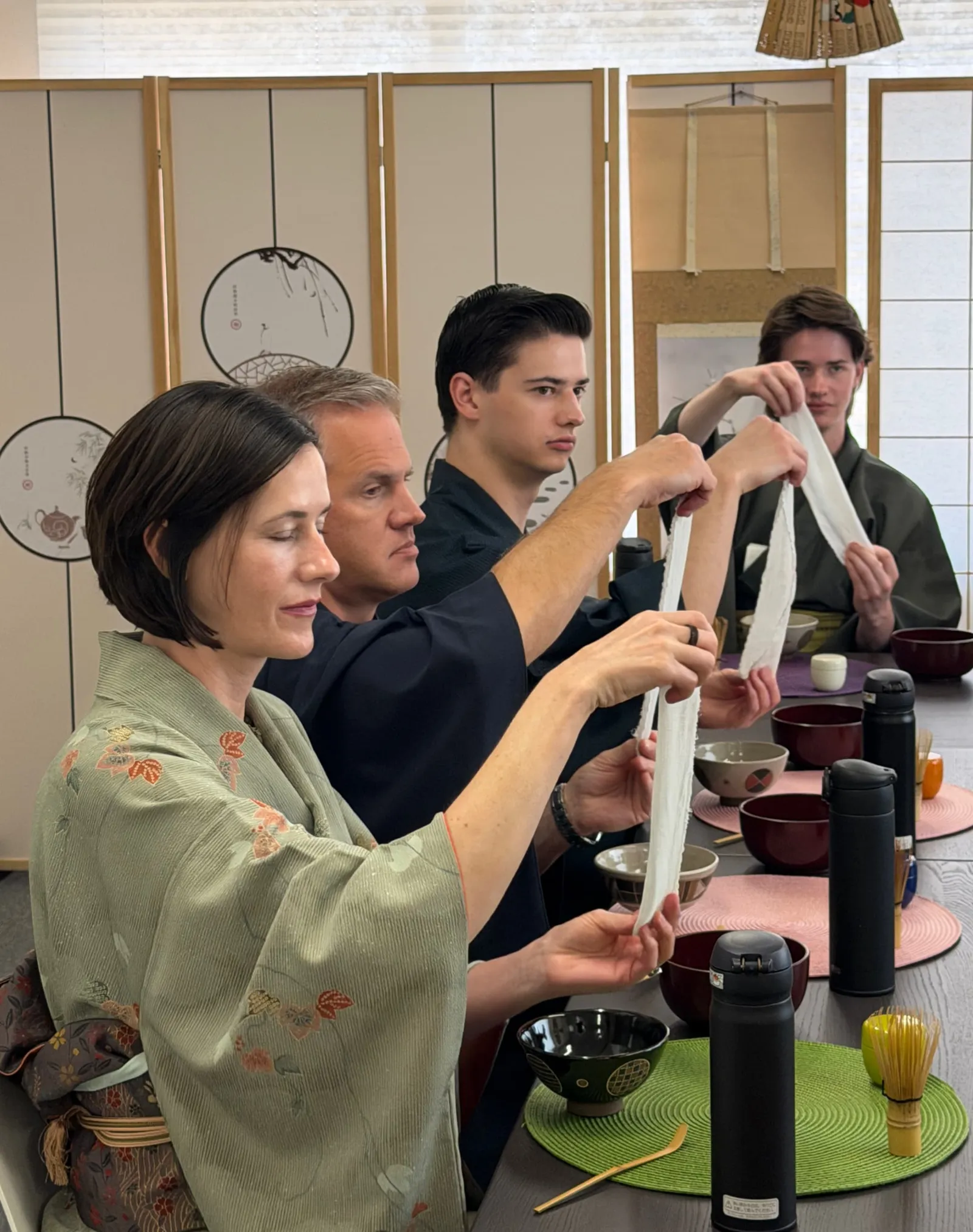 Four participants in kimono holding out white tea cloths with both hands