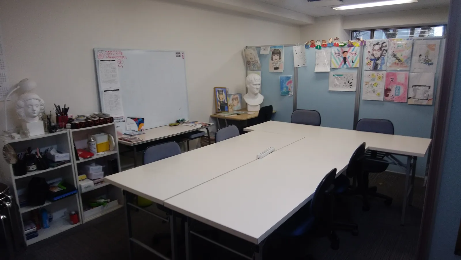 A classroom with white desks and chairs, with student artwork and plaster statues displayed on the walls
