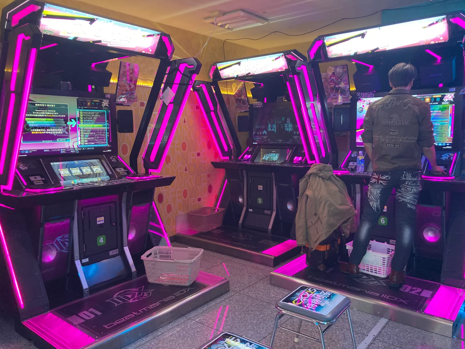 ピンクに光る音楽ゲームの筐体が並び、男性がプレイする様子