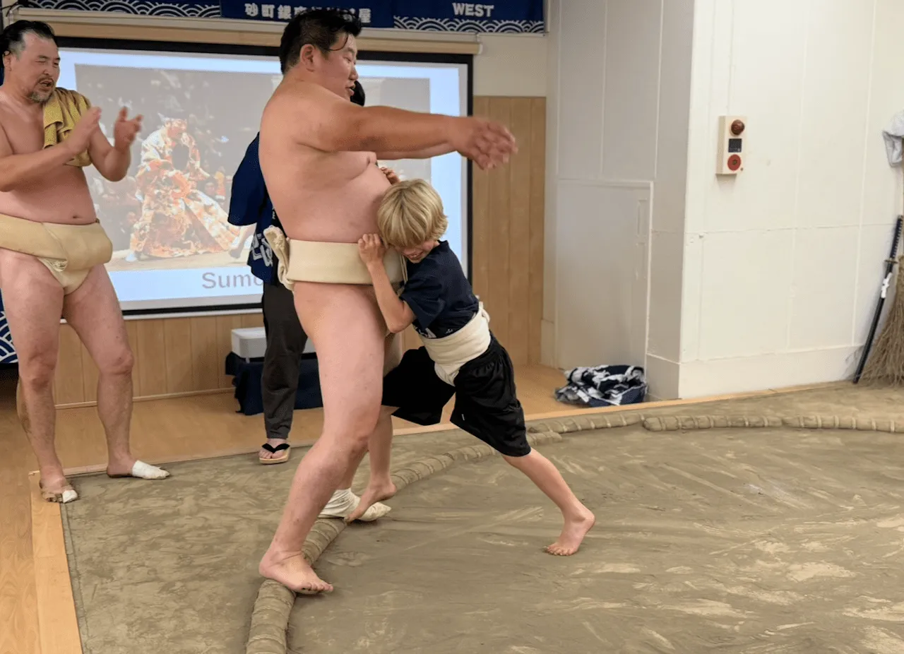 A child gripping a wrestler's mawashi and trying to push him back