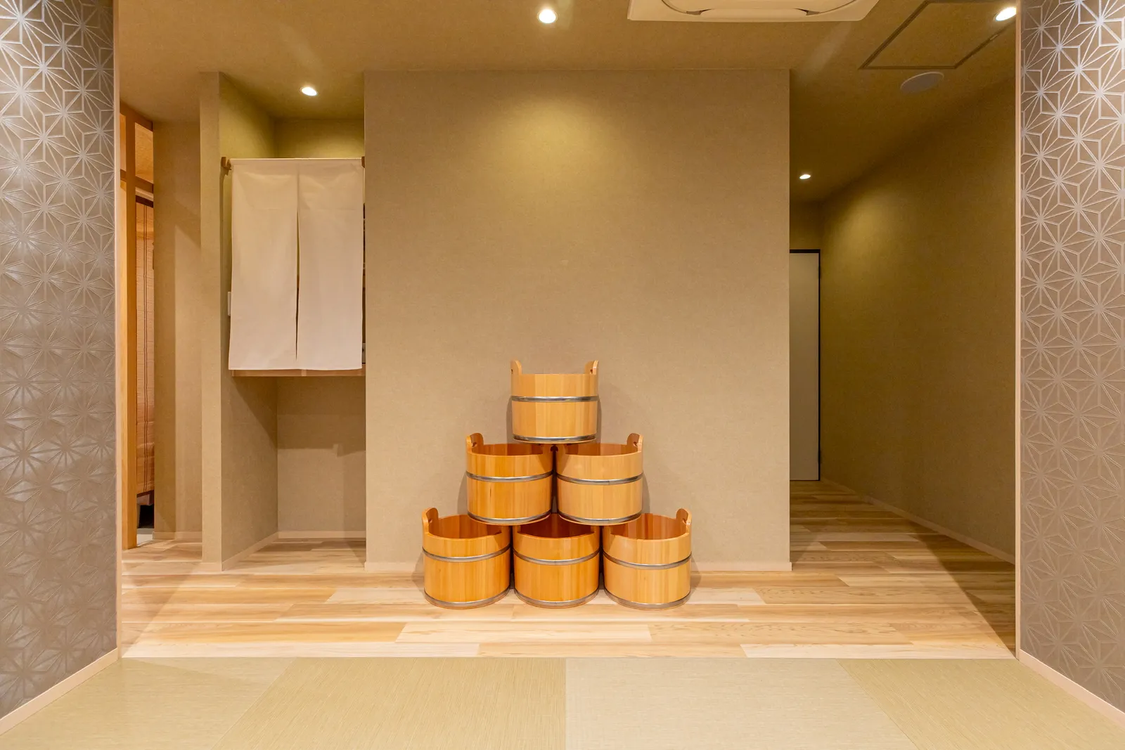 Stacked wooden buckets and a noren curtain in a space with tatami and a wooden floor