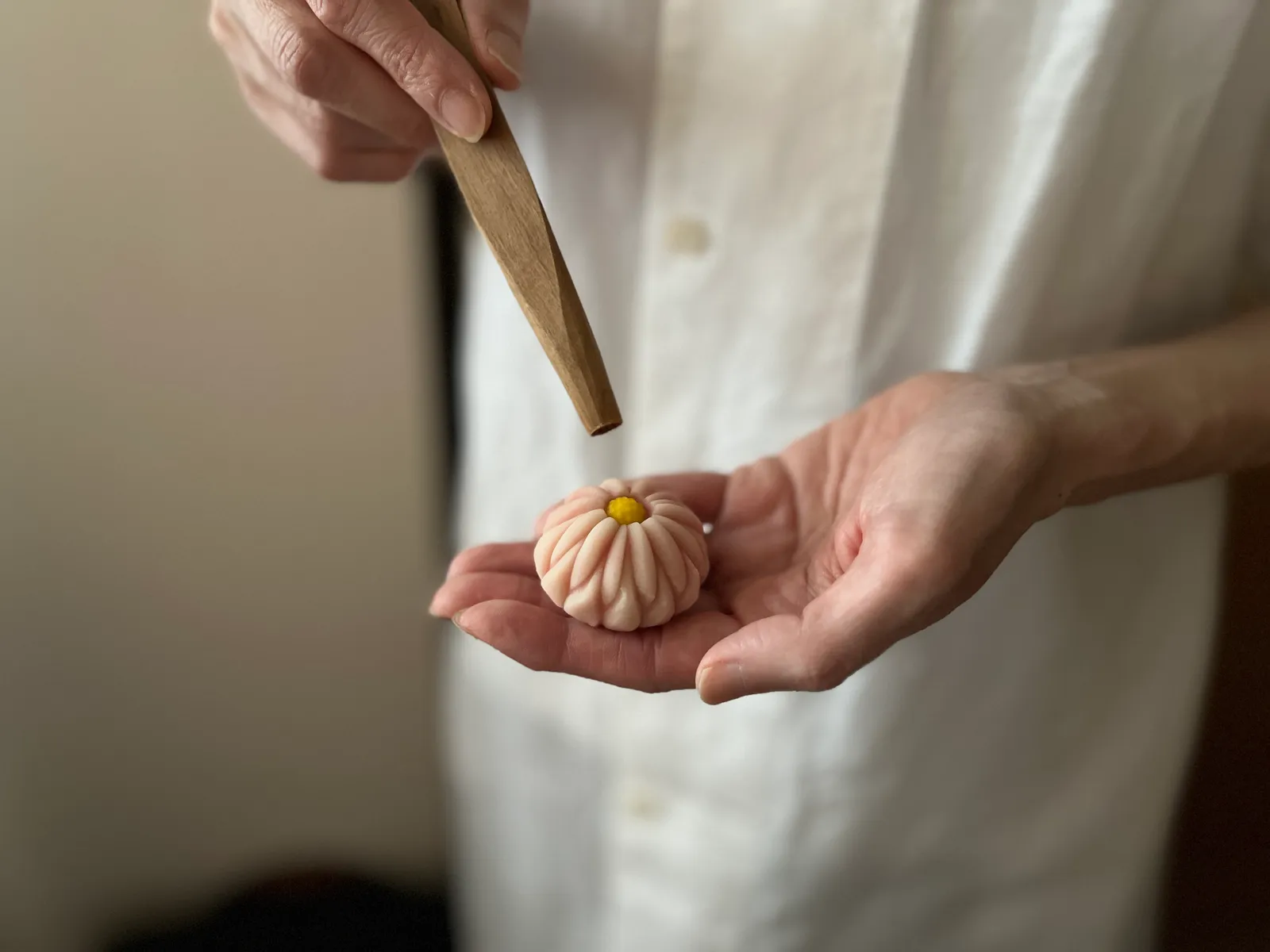 手のひらの上の菊形の練切と、三角ヘラを持つもう一方の手