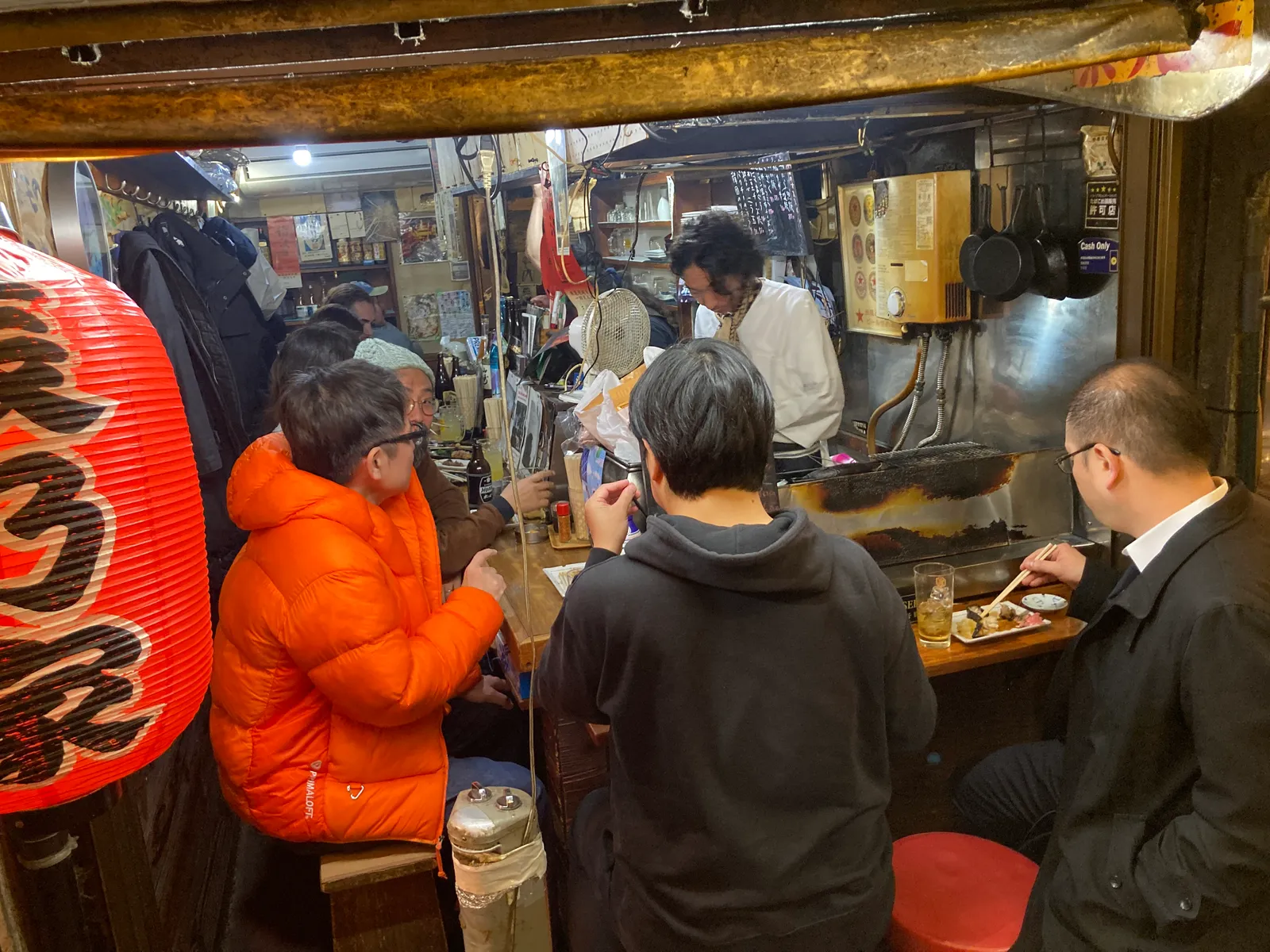 小さな店のカウンターに客が並び、店主が焼き台の前に立つ