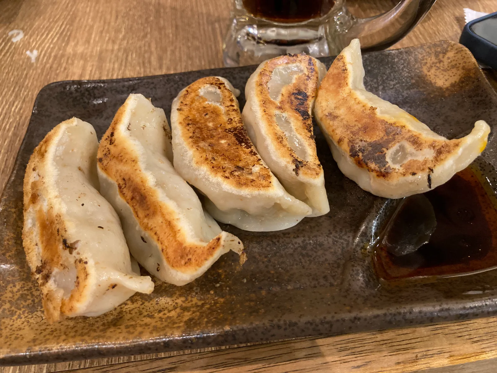 焼き色のついた餃子5個と黒い角皿、たれの小皿