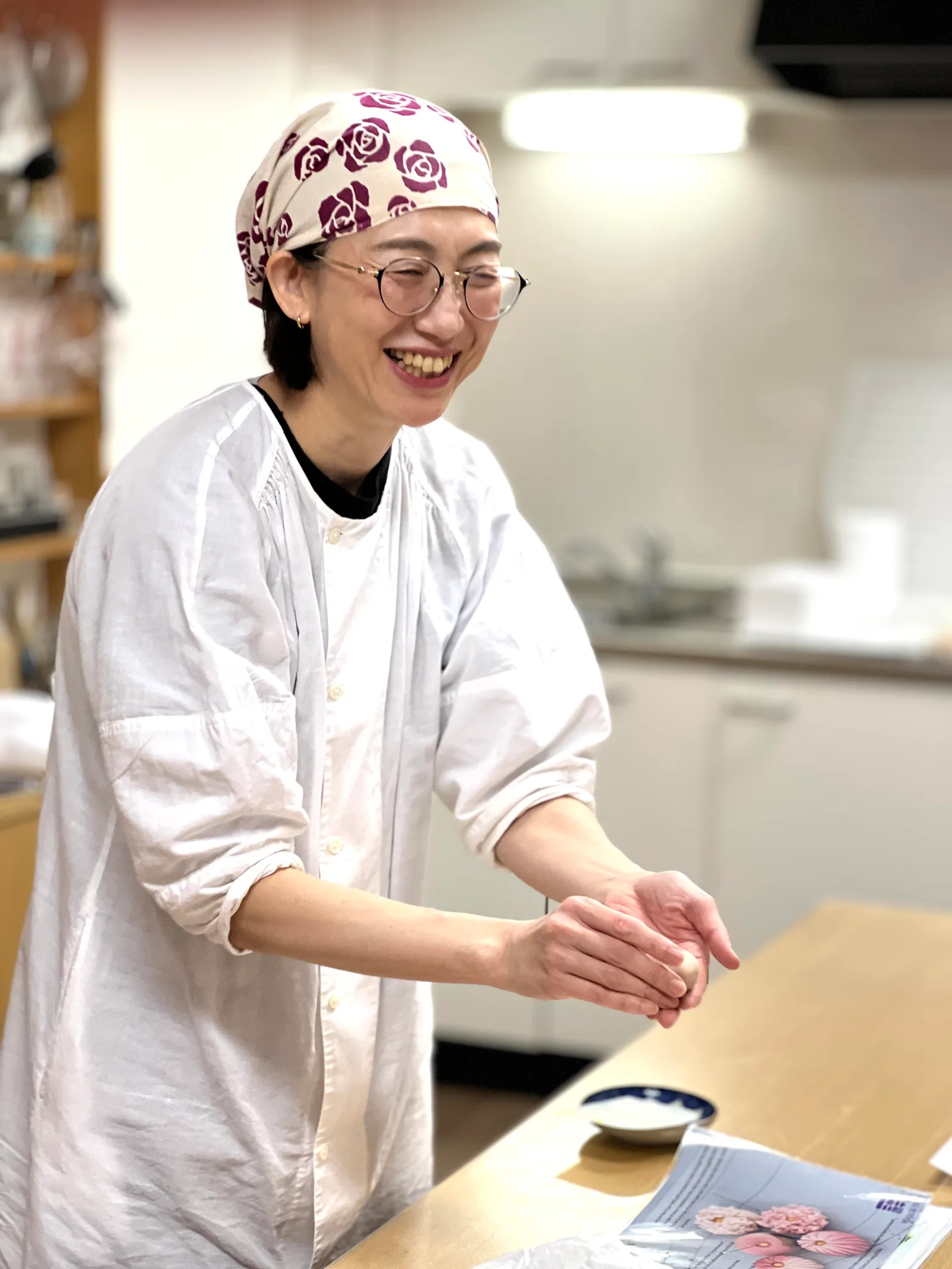 三角巾を着けた和菓子講師が両手で生地を丸めながら笑う様子