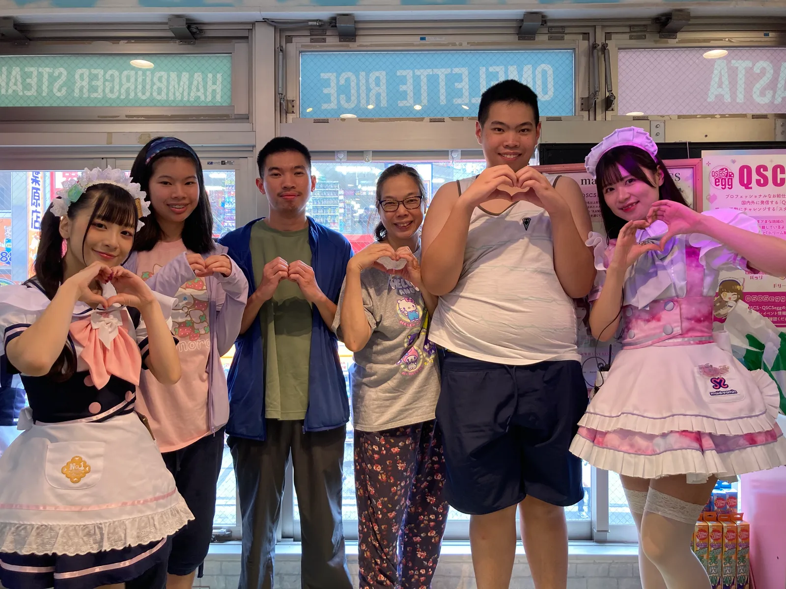 店頭でメイド2人と家族4人がハートポーズをそろえて並ぶ様子