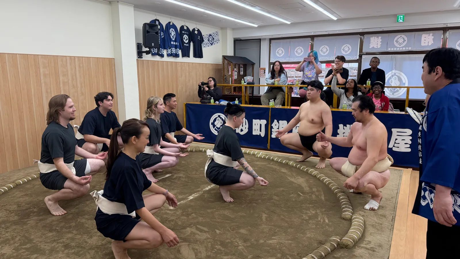 Participants wearing mawashi lowering their hips in the ring to learn basic movements
