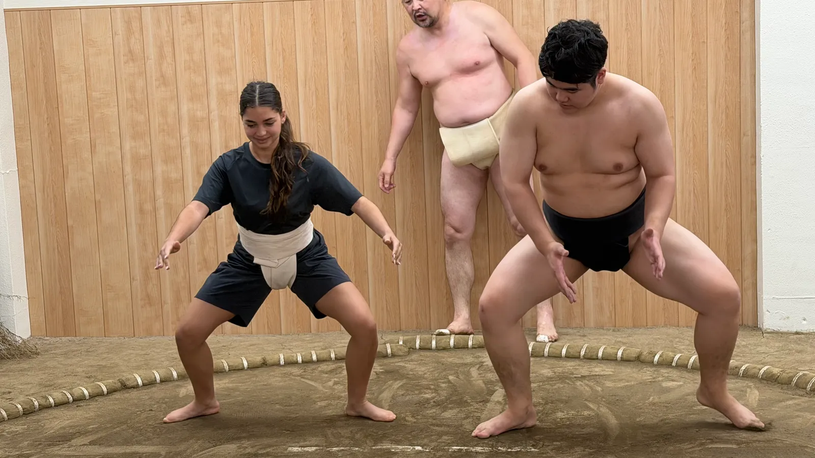 A participant standing beside a wrestler in the shiko stance