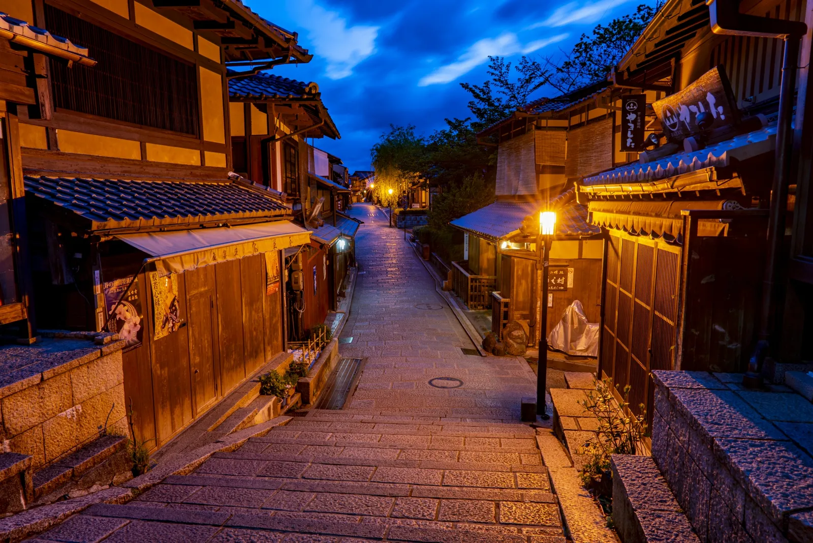 A deserted stone-stepped slope and machiya lit by street lamps