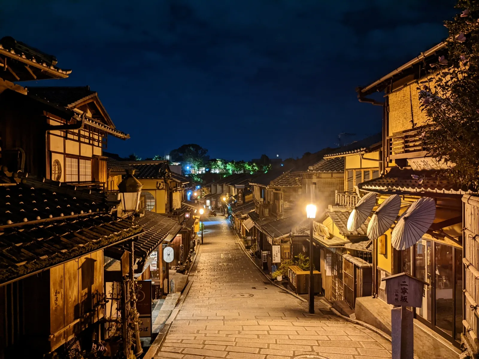 A night-time stone-paved street in Ninenzaka lined with signs and traditional paper parasol decorations