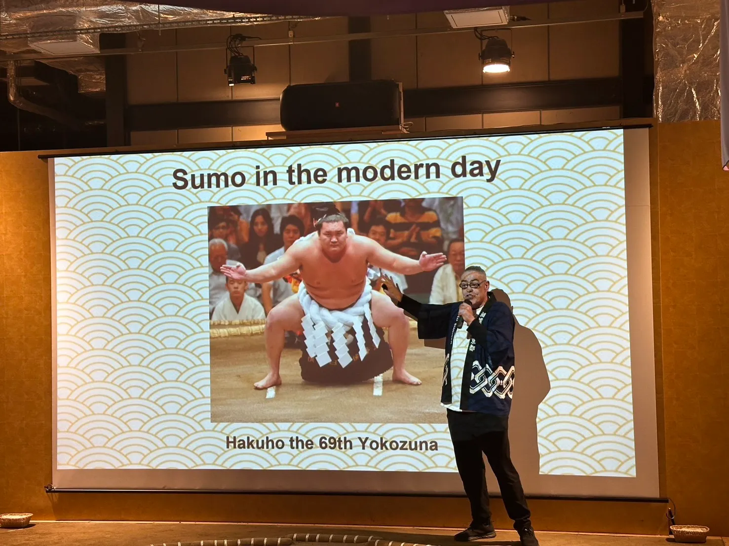 スクリーンに横綱の写真を映しながらマイクで解説するMC