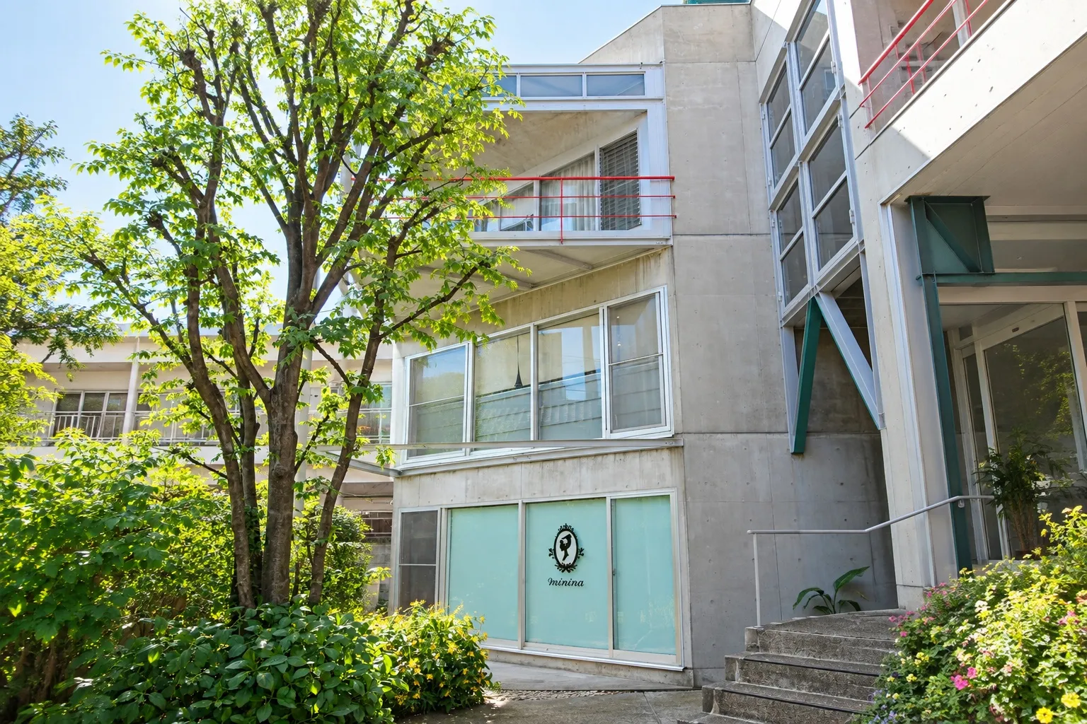 緑と花壇に囲まれたコンクリート造の建物とミニーナのロゴ看板