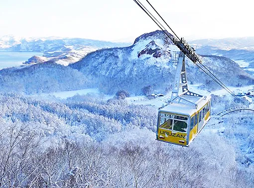 눈 덮인 산림 위를 지나가는 우스산 로프웨이의 노란 곤돌라