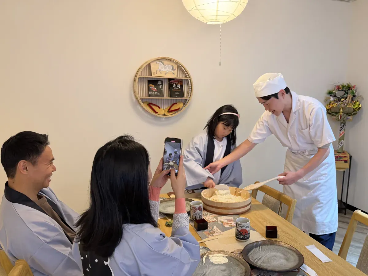 講師に教わりながら飯台を前にする法被姿の子どもと家族