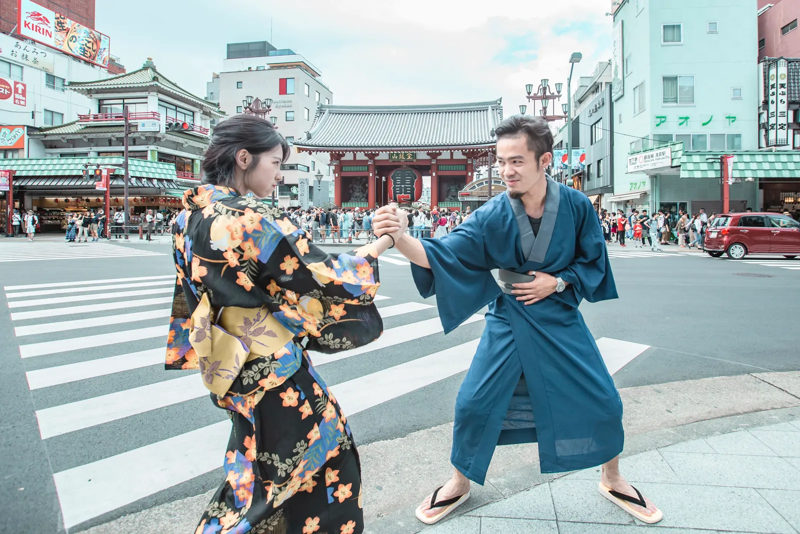 A couple in kimono posing hand in hand in front of Kaminarimon Gate