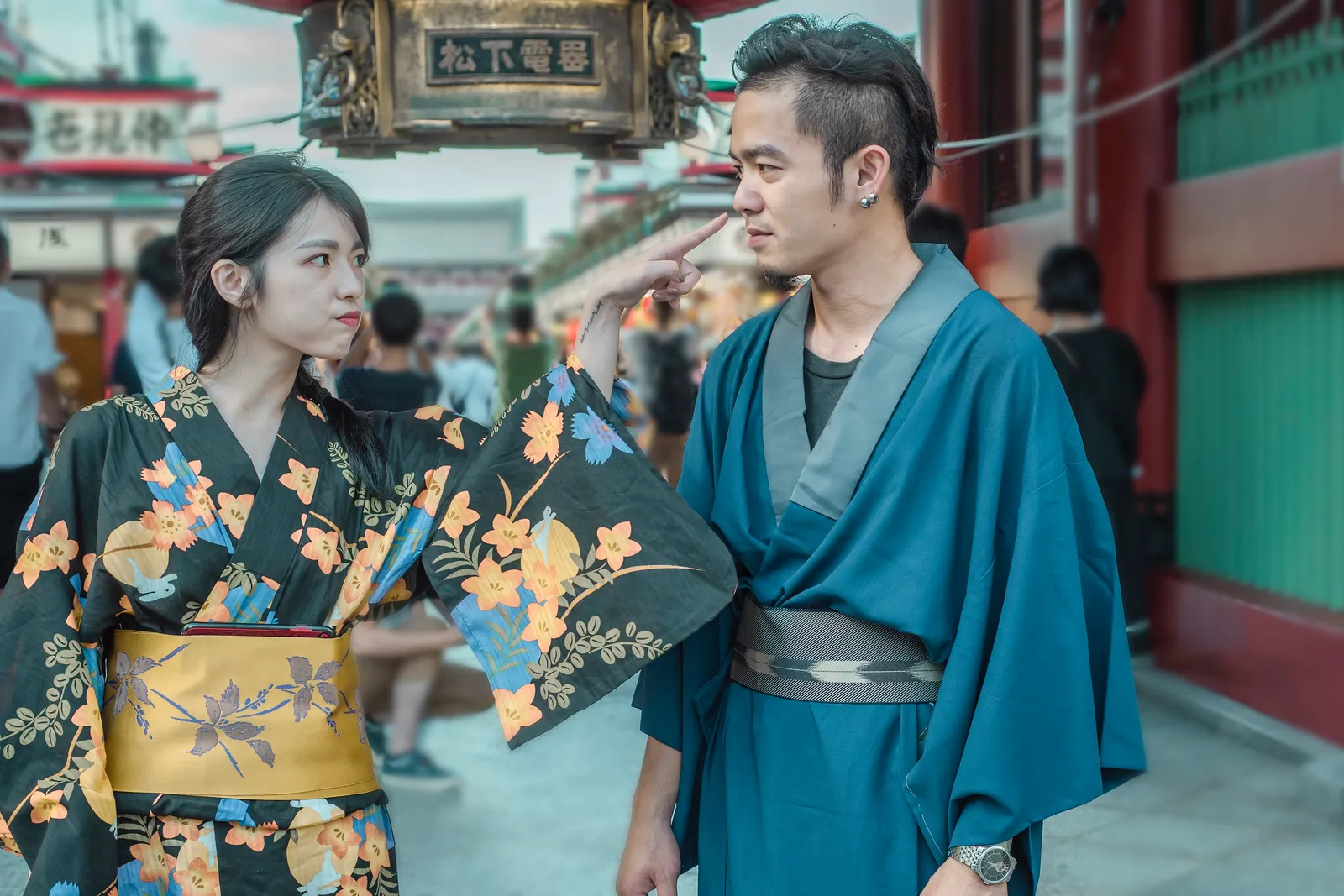 A woman in a floral kimono poking the cheek of a man in a blue kimono with her finger