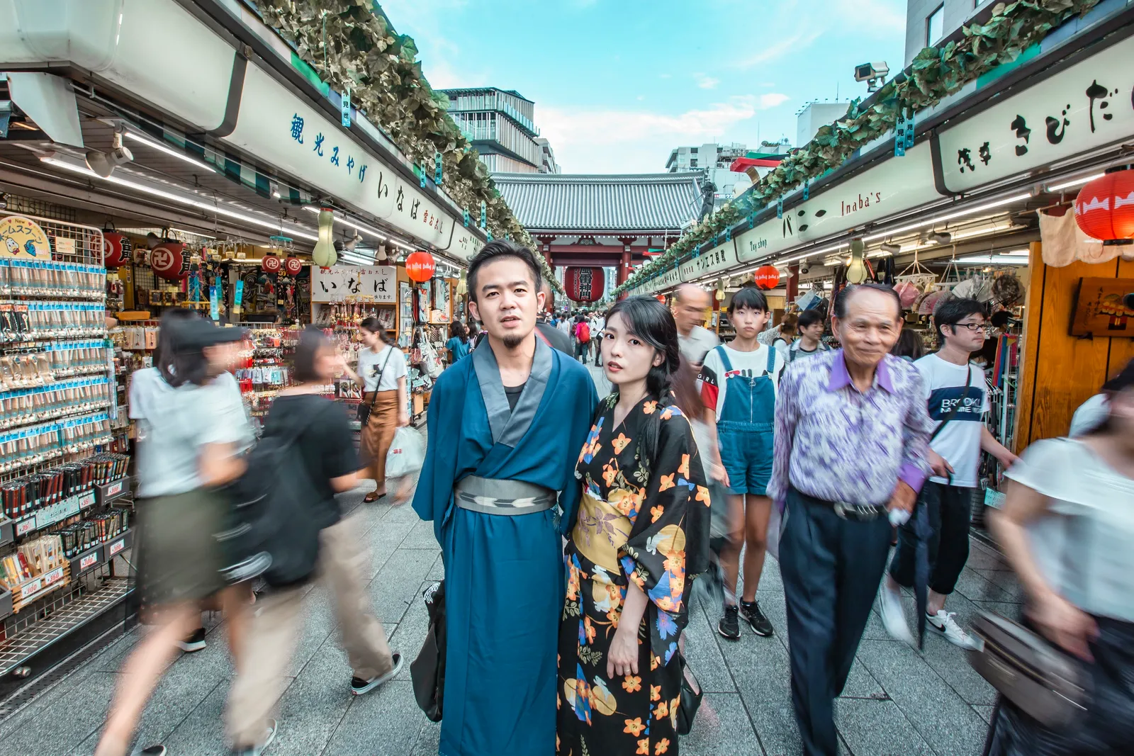 A couple in kimono standing on Nakamise Street, with the movement of passing crowds behind them