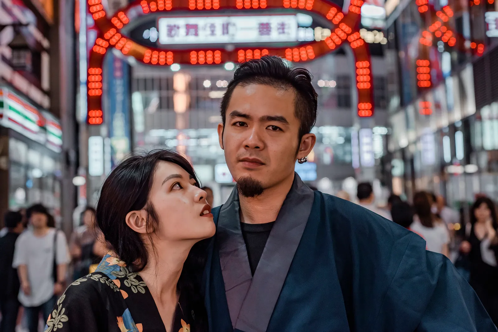 A couple in kimono snuggling close in front of the red neon arch in Kabukicho, Shinjuku
