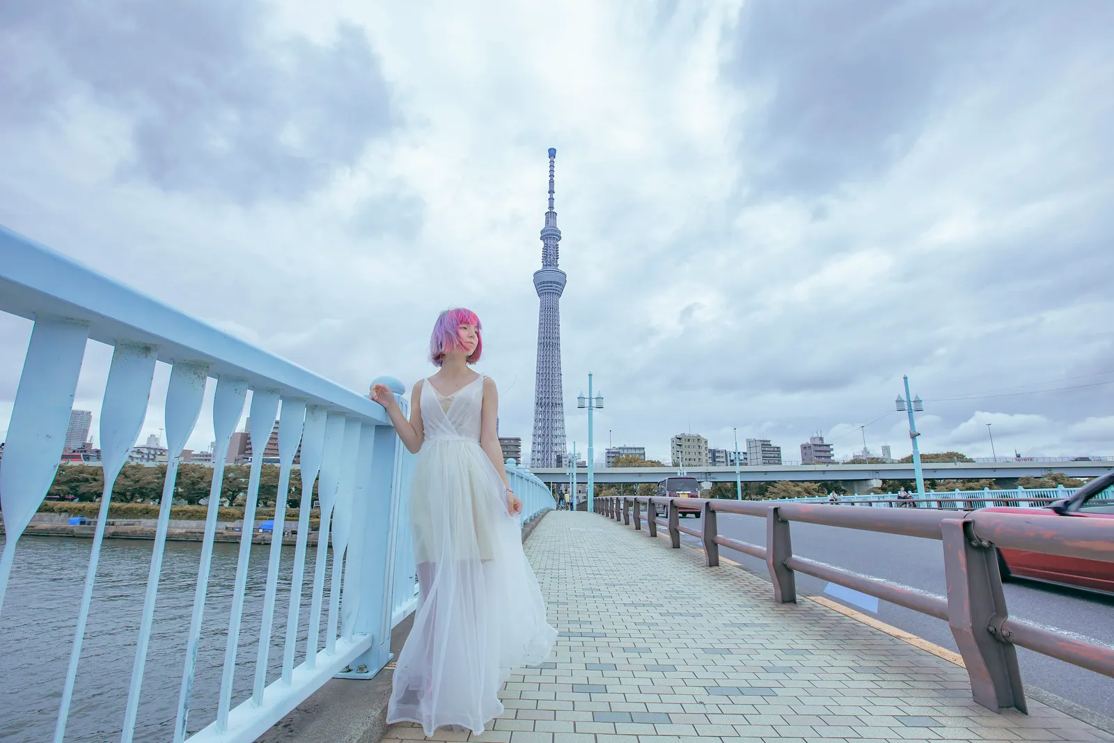 A woman standing in a white dress on a bridge with Tokyo Skytree in view