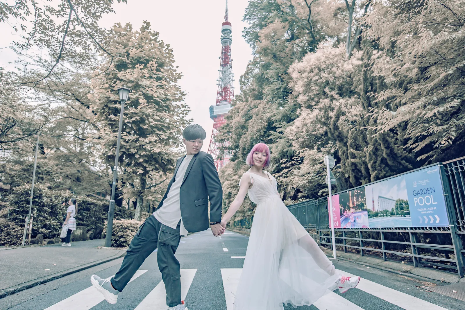 A woman in a white dress and a man in a black jacket holding hands with Tokyo Tower behind them