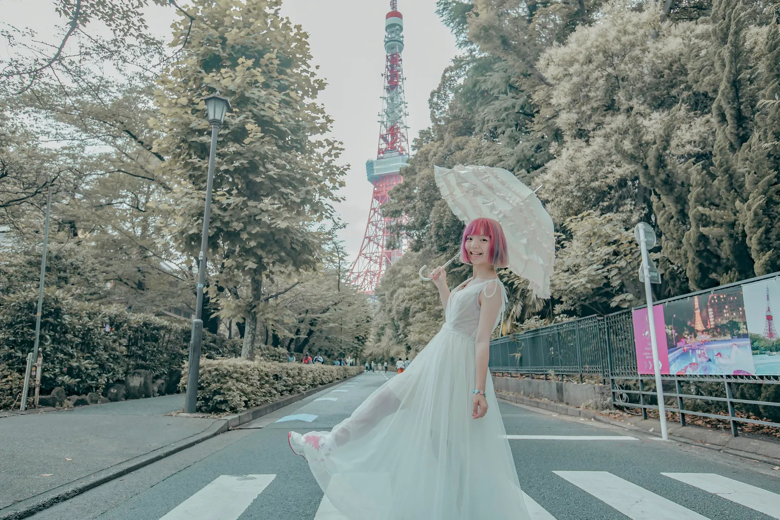 A woman in a dress holding a white parasol on a tree-lined path with Tokyo Tower in view