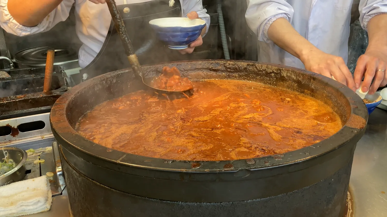 큰 철제 냄비에서 끓인 요리를 작은 그릇에 덜어주는 점원