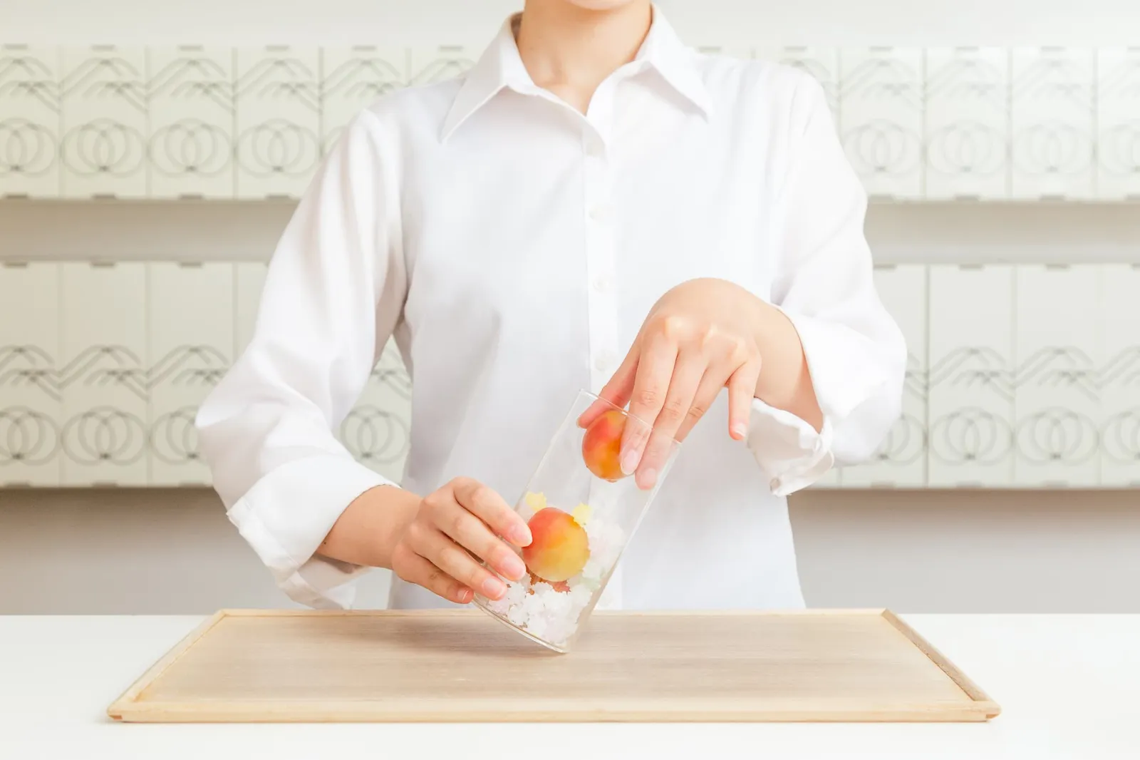 흰 셔츠를 입은 여성이 설탕을 깐 유리병에 매실을 넣는 손동작