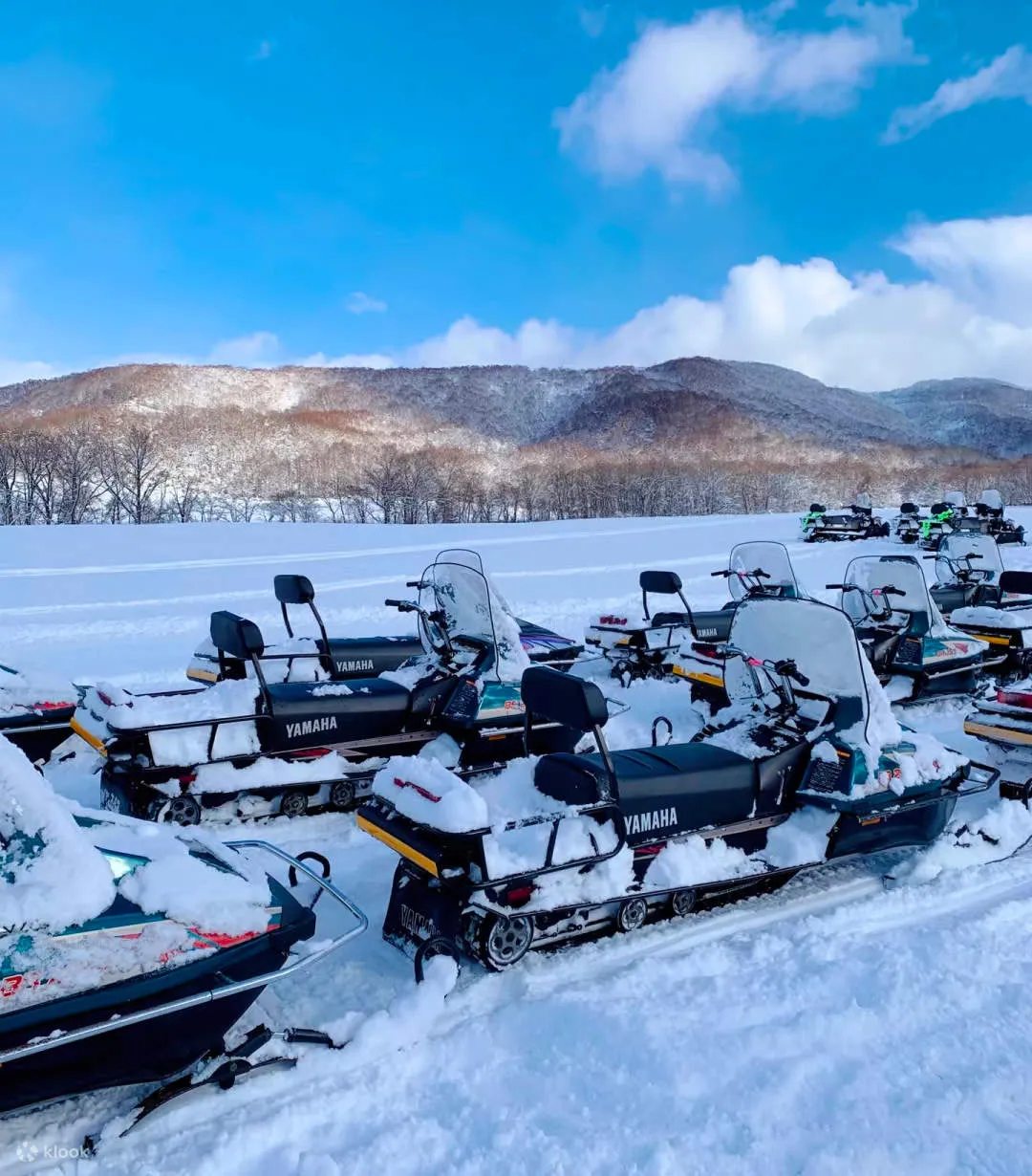 雪原に並ぶヤマハのスノーモービル数台と背後の雪山